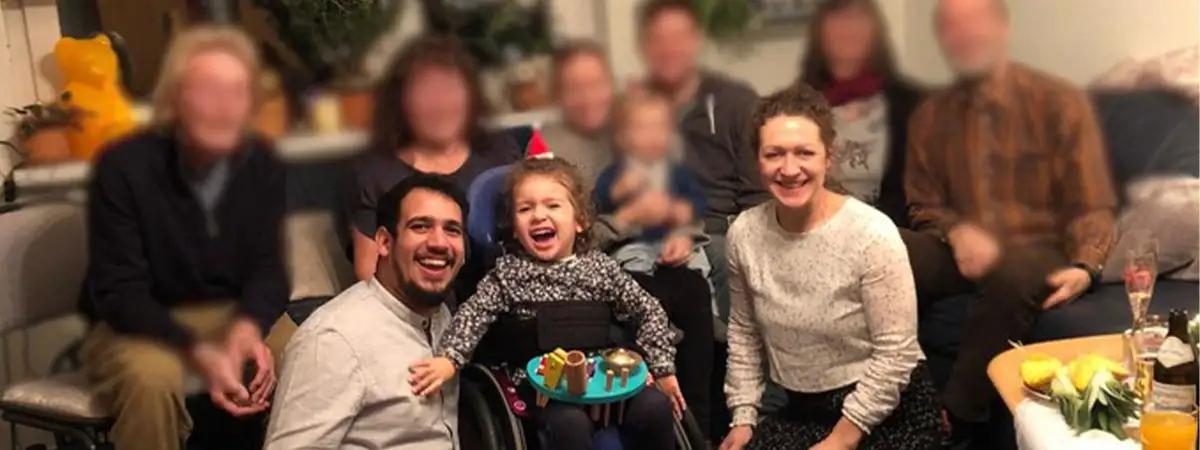 Familienportrait: Auf dem Bild sind mehrere Familienmitglieder zu sehen. Darunter auch die kleine SMA-Patientin und ihre Eltern. Die Personen sitzen im Wohnzimmer auf dem Sofa und dem Boden und lachen in die Kamera.