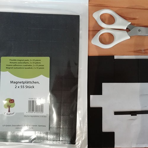 Eine Verpackung mit Magnetplättchen, 2 x 55 Stück, eine weiße Bastelschere und eine angebrochene Packung mit Magnetplättchen sind zu sehen.