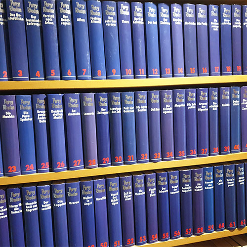 Im Holzregal stehen 64 blaue Bände einer Buchreihe.