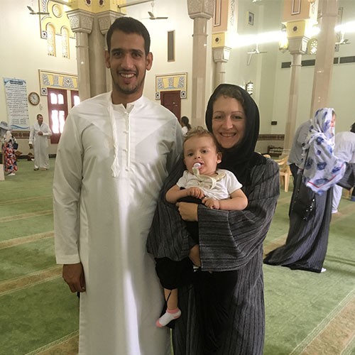 Familienfoto aus dem Urlaub in Dubai: Der Vater trägt ein weißes Gewand. Die Mutter trägt ein schwarzes Gewand mit Kopftuch und hält ihr Kleinkind im Arm.