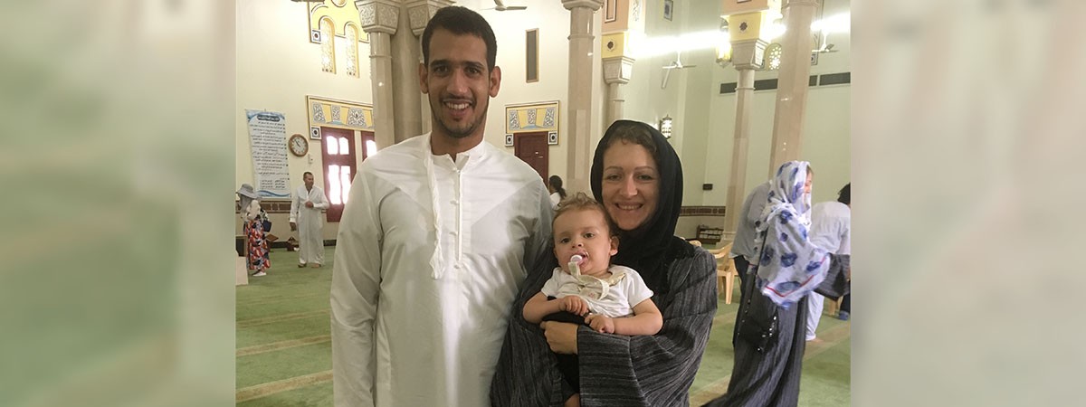 Familienfoto aus dem Urlaub in Dubai: Der Vater trägt ein weißes Gewand. Die Mutter trägt ein schwarzes Gewand mit Kopftuch und hält ihr Kleinkind im Arm.