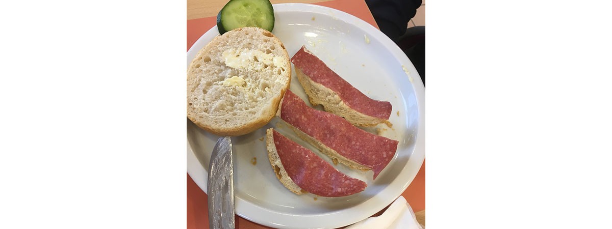 Auf einem Teller liegen eine Brötchenhälfte sowie eine in drei Streifen geschnittene Brötchenhälfte, die mit einer Salamischeibe belegt ist.