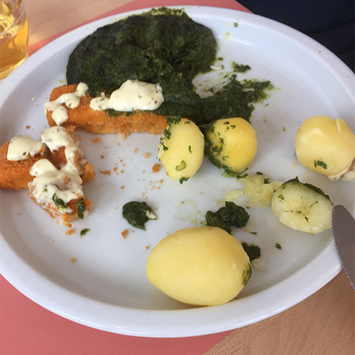 Auf einem Teller liegen Kartoffeln, Fischstäbchen mit Sauce sowie Spinat.