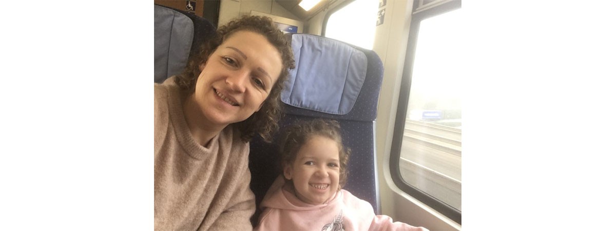 Mutter und Tochter mit SMA schauen lächelnd in die Kamera während sie mit dem Zug reisen.