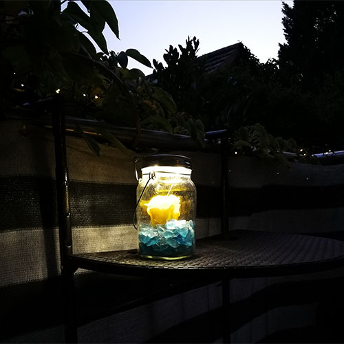 Kerze im Glas bei Dunkelheit auf einem halbrunden kleinen Tisch auf dem Balkon
