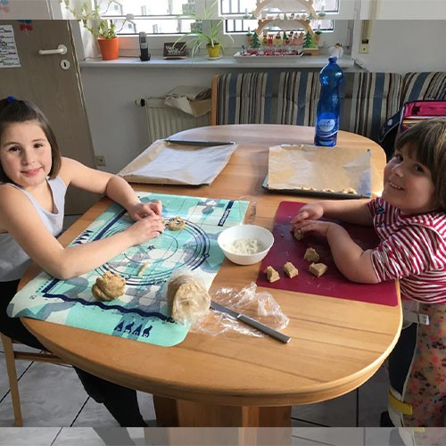 Die kleine sechsjährige SMA-Patientin und ihre große Schwester sitzen sich gegenüber an einem Tisch und kneten und formen einen Plätzchenteig.