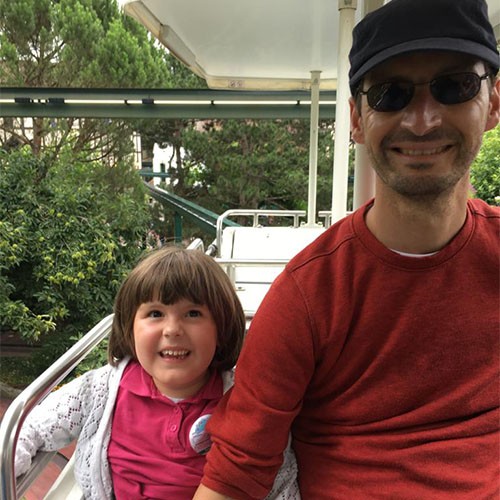 Ein Vater mit seiner kleinen Tochter, die SMA-Patientin ist, sitzen in einem Fahrgeschäft in einem Freizeitpark und haben sichtlich Spaß.