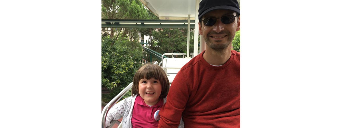 Ein Vater mit seiner kleinen Tochter, die SMA-Patientin ist, sitzen in einem Fahrgeschäft in einem Freizeitpark und haben sichtlich Spaß.
