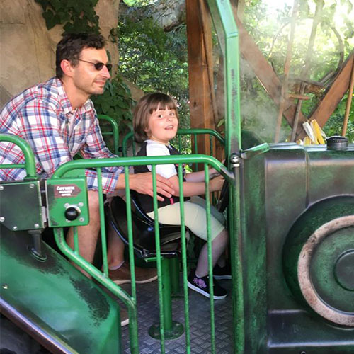 Die kleine SMA-Patientin sitzt mit ihrem Vater in einem Fahrgeschäft in einem Freizeitpark.