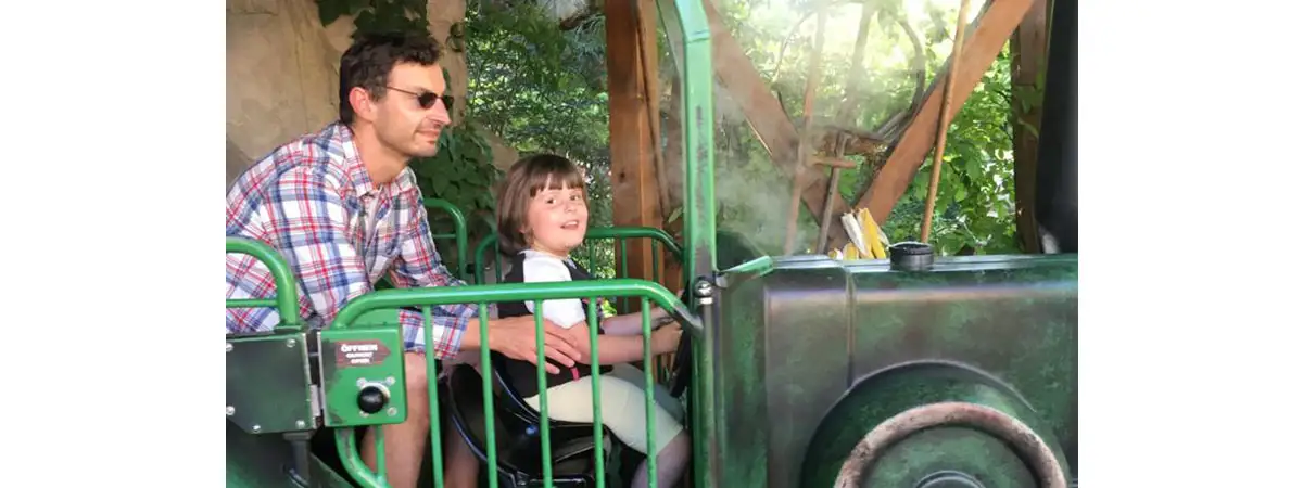 Die kleine SMA-Patientin sitzt mit ihrem Vater in einem Fahrgeschäft in einem Freizeitpark.