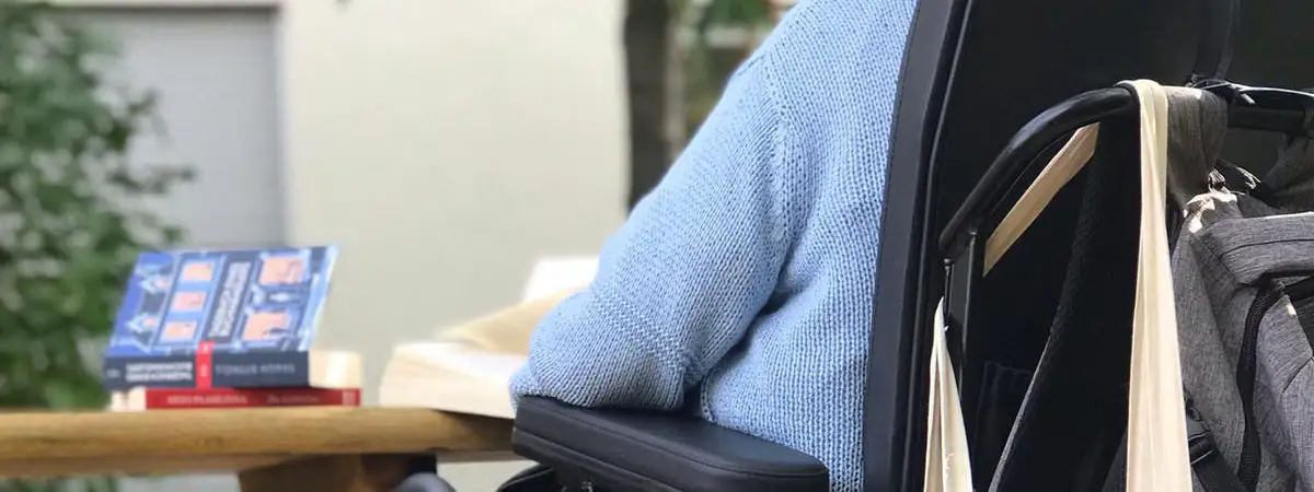 Patientin sitzt mit dem Rücken zum Betrachter in einem Rollstuhl am Tisch und liest ein Buch.