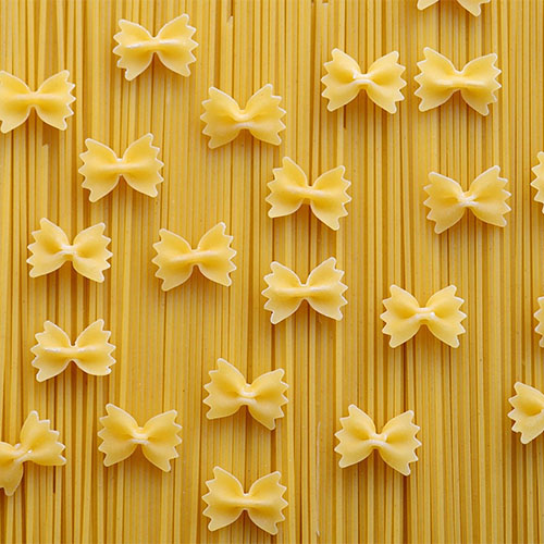 Ungekochte Nudeln sind zu sehen: Auf Spaghetti-Nudeln wurde dekorativ Farfalle, Nudeln in Schmetterlingsform, drapiert.