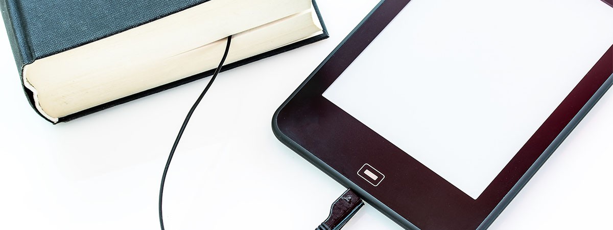 Ein Tablet oder E-Reader wird mit einem Ladekabel geladen. Das Ende des Kabels steckt in einem Buch.