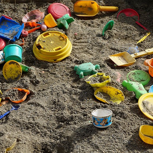 In einem Sandkasten für Kinder liegen bunte Sandspielzeuge wie Schaufeln, Förmchen und ein Sieb.