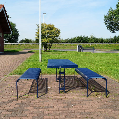 Raststätte mit Wiese und blauem Tisch mit Sitzgelegenheiten sowie einem Toilettenhäuschen mit Behindertensymbol im Hintergrund.