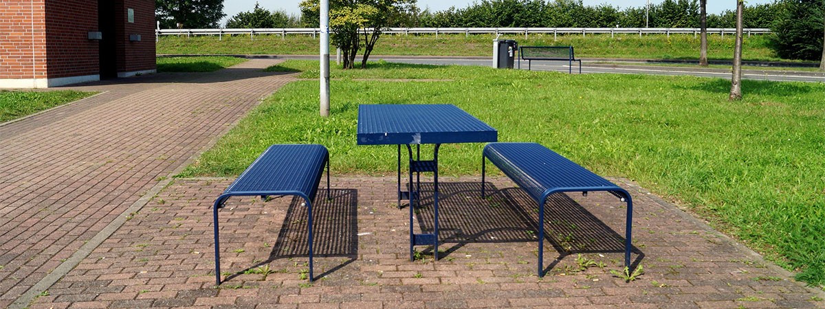 Raststätte mit Wiese und blauem Tisch mit Sitzgelegenheiten sowie einem Toilettenhäuschen mit Behindertensymbol im Hintergrund.