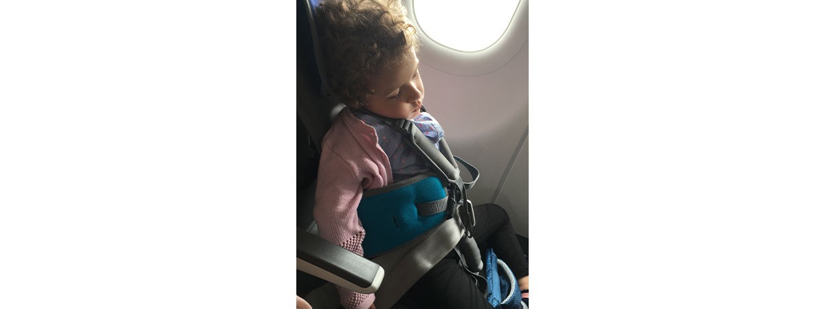 Das kleine Mädchen mit SMA Typ 1 sitzt schlafend auf einem speziellen Kindersitz im Flugzeug.