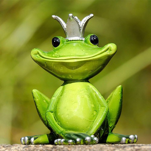 Eine Gartenfigur sitzt auf einer Mauer. Der grüne Frosch stellt eine Märchenfigur dar und trägt eine Krone.