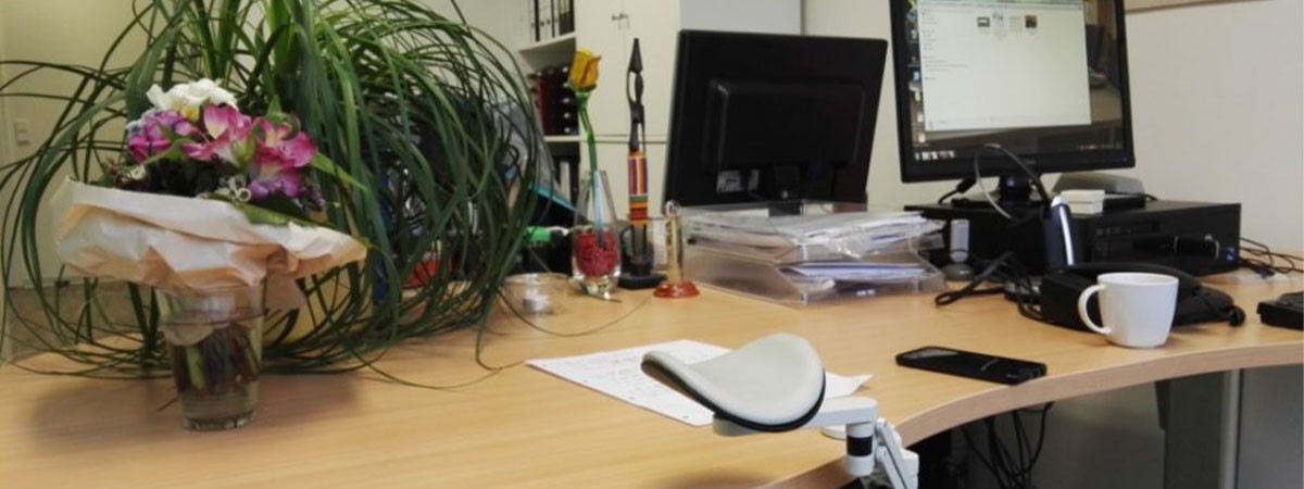 Auf einem Schreibtisch im Büro stehen Arbeitscomputer und weitere Gegenstände eines Arbeitsplatzes.