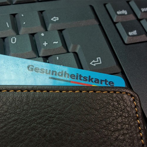 Eine Versichertenkarte der Krankenkasse mit der Aufschrift "Gesundheitskarte" steckt in einem Portemonnaie, das auf einer Tastatur liegt.