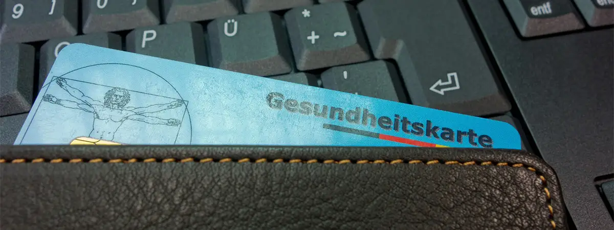 Eine Versichertenkarte der Krankenkasse mit der Aufschrift "Gesundheitskarte" steckt in einem Portemonnaie, das auf einer Tastatur liegt.