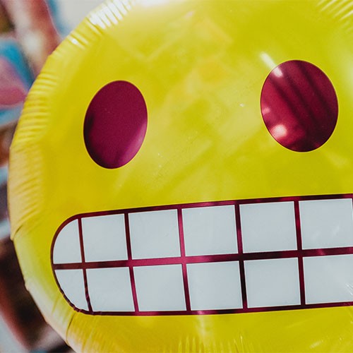 Gelber Smiley-Luftballon grinst ängstlich und zeigt dabei Zähne.