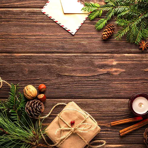 Ein weihnachtlich dekorierter Tisch mit Tannenbaumzweig und Tannenzapfen, Briefumschlag, Kerze, Zimt, Nüssen und einem Geschenk.