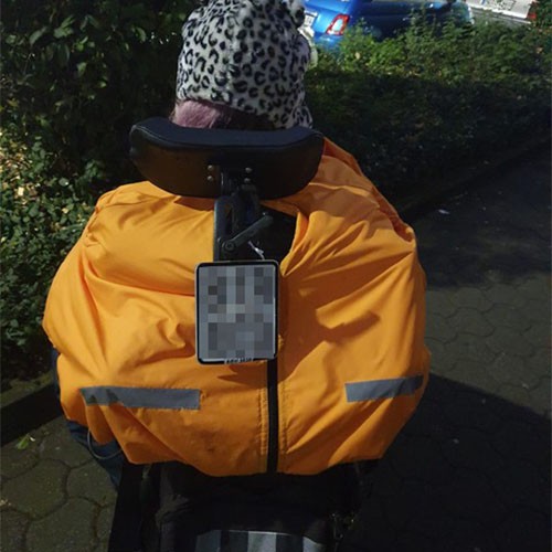 Eine SMA-Patientin sitzt draußen im Rollstuhl mit dem Rücken zur Kamera. Sie trägt Winterkleidung: eine warme Mütze sowie eine spezielle Daunenjacke für Rollstuhlfahrer.
