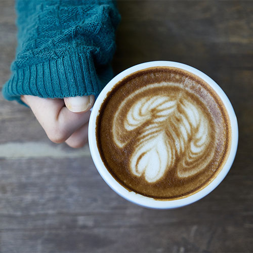 Eine Hand hält eine Kaffeetasse mit verziertem Milchschaum.