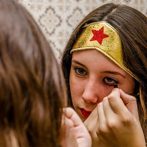 Ein Mädchen ist als Superheldin verkleidet, schaut in den Spiegel und schminkt sich.
