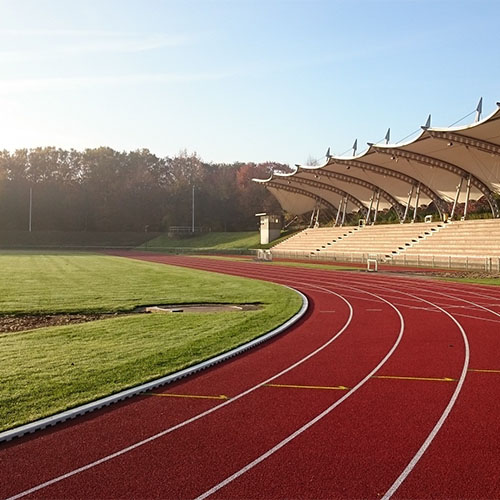 Rote Tartanbahn zum Laufen, ein Sportplatz und eine Zuschauertribüne.