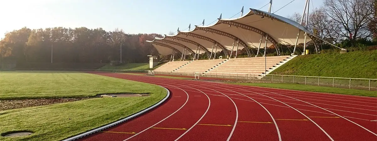 Rote Tartanbahn zum Laufen, ein Sportplatz und eine Zuschauertribüne.