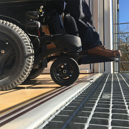 Die Räder eines Rollstuhls rollen über die stufenlose Schwelle der Tür zum Balkon.