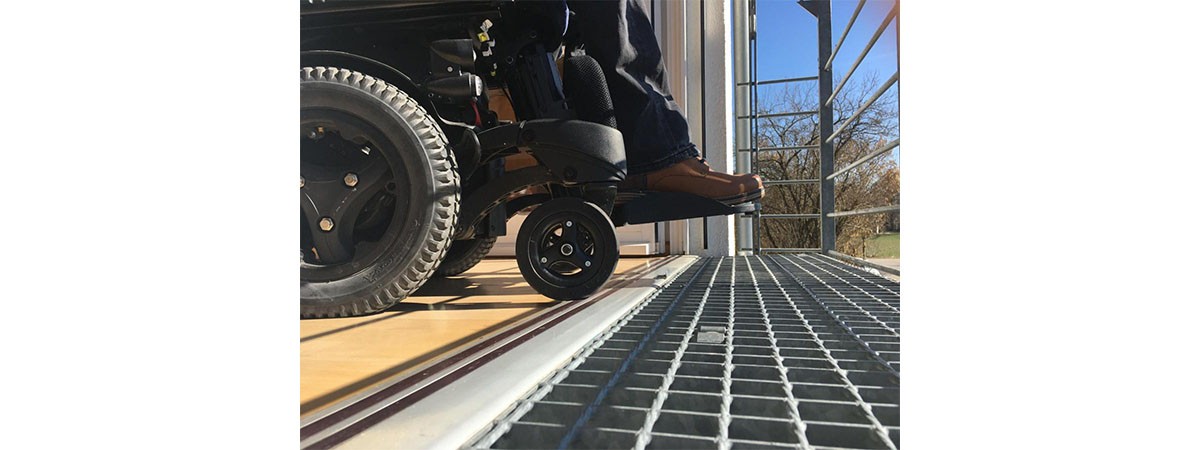 Die Räder eines Rollstuhls rollen über die stufenlose Schwelle der Tür zum Balkon.