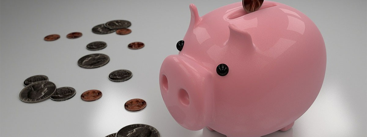 Ein rosa Sparschwein, das lächelt und darüber eine Hand, die eine Geldmünze in die Spardose steckt.