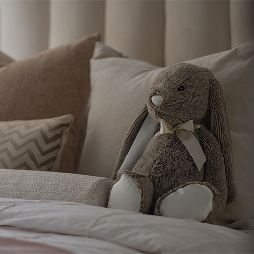 Ein Bett mit weißen und beigen Kissen und Decken und einem Kuscheltier-Hasen.