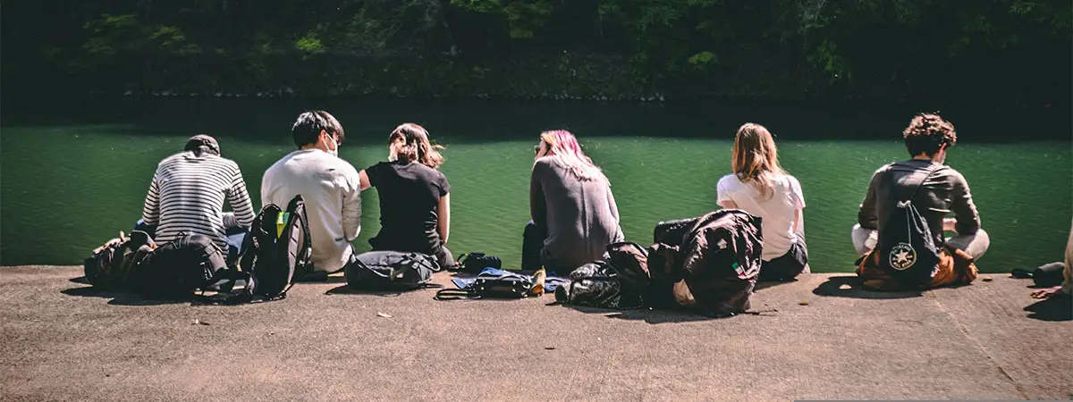 Eine Gruppe von Freunden verbringt ihre Freizeit gemeinsam an einem See. Die Jugendlichen sitzen in der Sonne und schauen aufs Wasser.