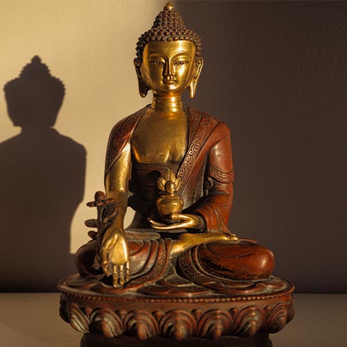 Goldene Buddha Statue, die im Schneidersitz sitzt und meditiert und einen Schatten an die Wand wirft.