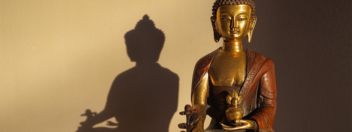Goldene Buddha Statue, die im Schneidersitz sitzt und meditiert und einen Schatten an die Wand wirft.