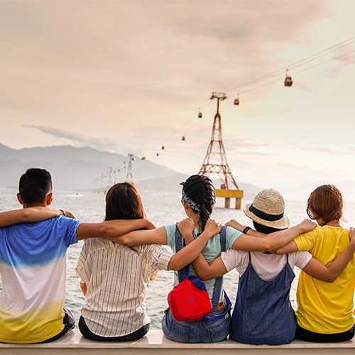 Acht Freunde sitzen Arm in Arm nebeneinander und blicken auf das Wasser. Die jungen Menschen halten sich gegenseitig unterstützend fest.