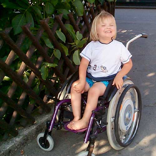 Die SMA-Patientin Amelie als Kind. Das Mädchen sitzt draußen im Rollstuhl und lächelt fröhlich.