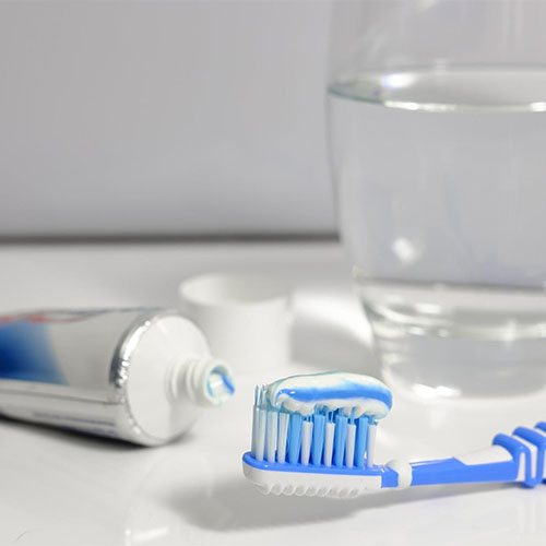 Artikel für die Mundhygiene: Eine Zahnpastatube, eine Zahnbürste und ein Glas Wasser zum Ausspülen.