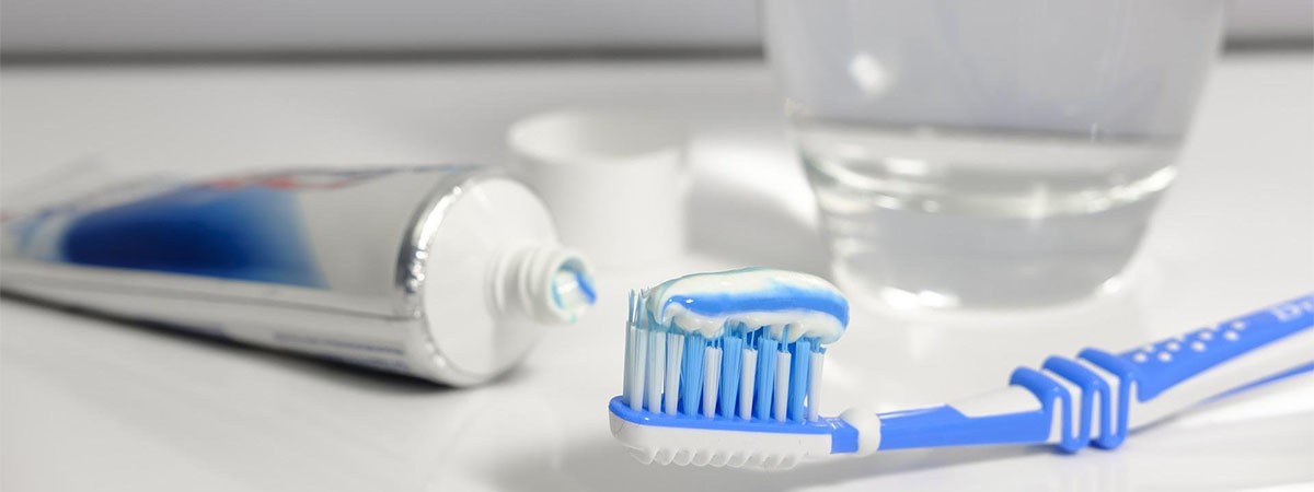 Artikel für die Mundhygiene: Eine Zahnpastatube, eine Zahnbürste und ein Glas Wasser zum Ausspülen.