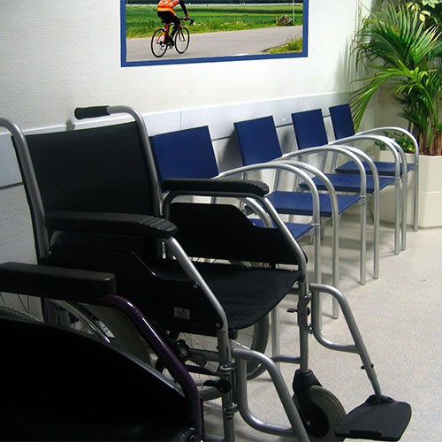 Warteraum einer Arztpraxis mit Stühlen und einem Rollstuhl
