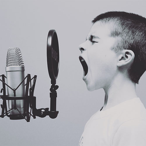 Ein Junge singt in ein Mikrophon, das seine Stimme aufnimmt.