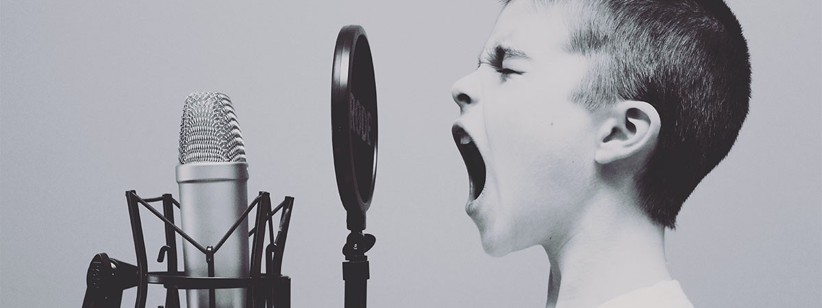 Ein Junge singt in ein Mikrophon, das seine Stimme aufnimmt.