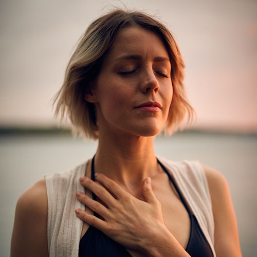 Eine Frau macht Atemübungen und hält eine Hand auf dem Brustkorb, um zu spüren, wie sich die Lungen füllen.