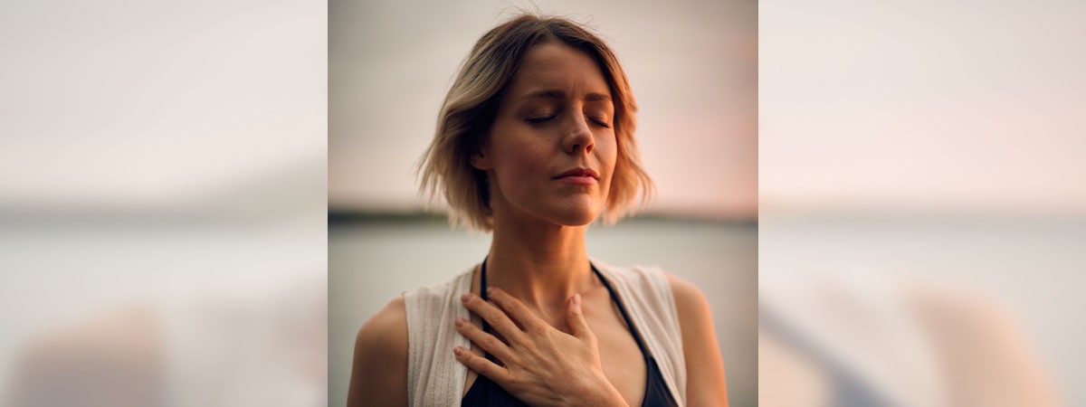Eine Frau macht Atemübungen und hält eine Hand auf dem Brustkorb, um zu spüren, wie sich die Lungen füllen.