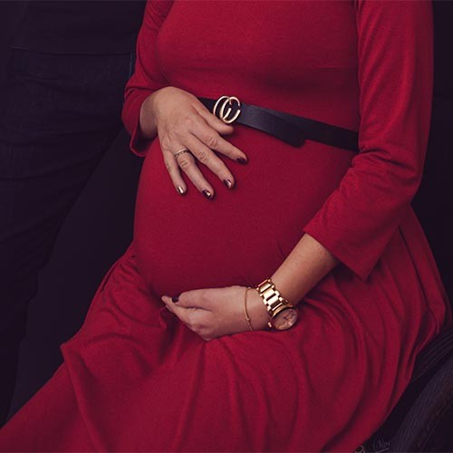 Der Bauch einer Schwangeren im Rollstuhl. Die Frau trägt ein rotes Kleid und hält ihren Bauch.