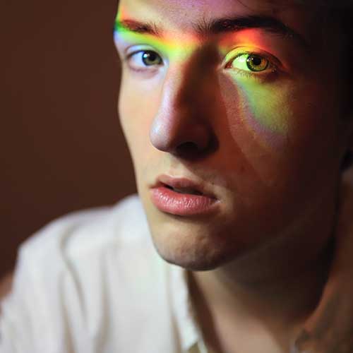 Ein Mann hat Lichtreflexe auf dem Gesicht, die einen Regenbogen formen. 